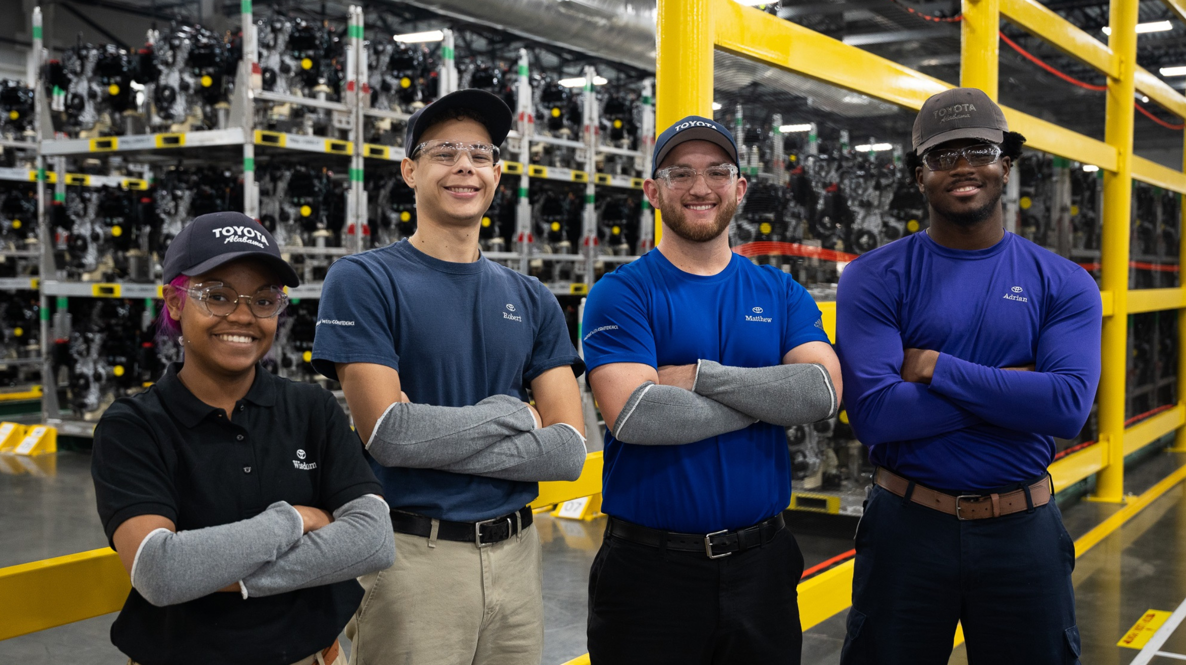 Four Toyota associates stand in front of manufacturing equipment with their arms crossed in front of their chests