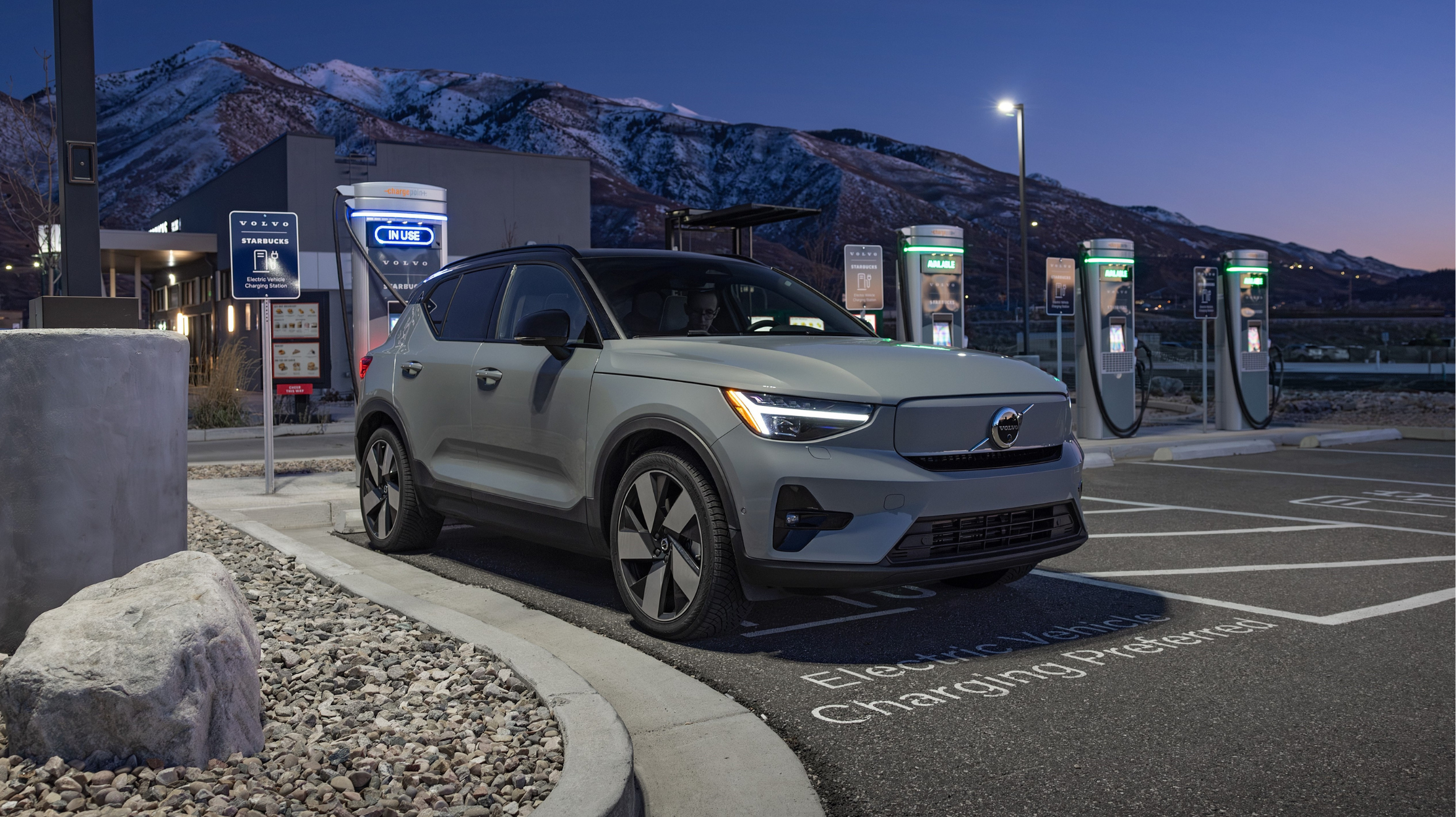 An electric Volvo vehicle sits in the parking lot of a Starbucks store connected to an electric vehicle charger